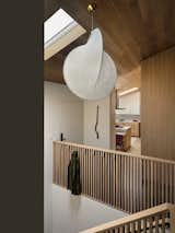 The custom slatted wood railings is fitted with discreet flip-down hooks to hang coats. Stairs lead down to a guest space and an additional unit for a future caretaker. An elevator, not visible, also connects the two levels. The Overlap pendant is by Michael Anastassiades for Flos.